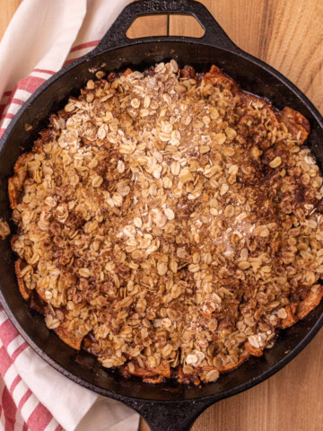 Baked apple crisp in a cast iron skillet with a red and white napkin