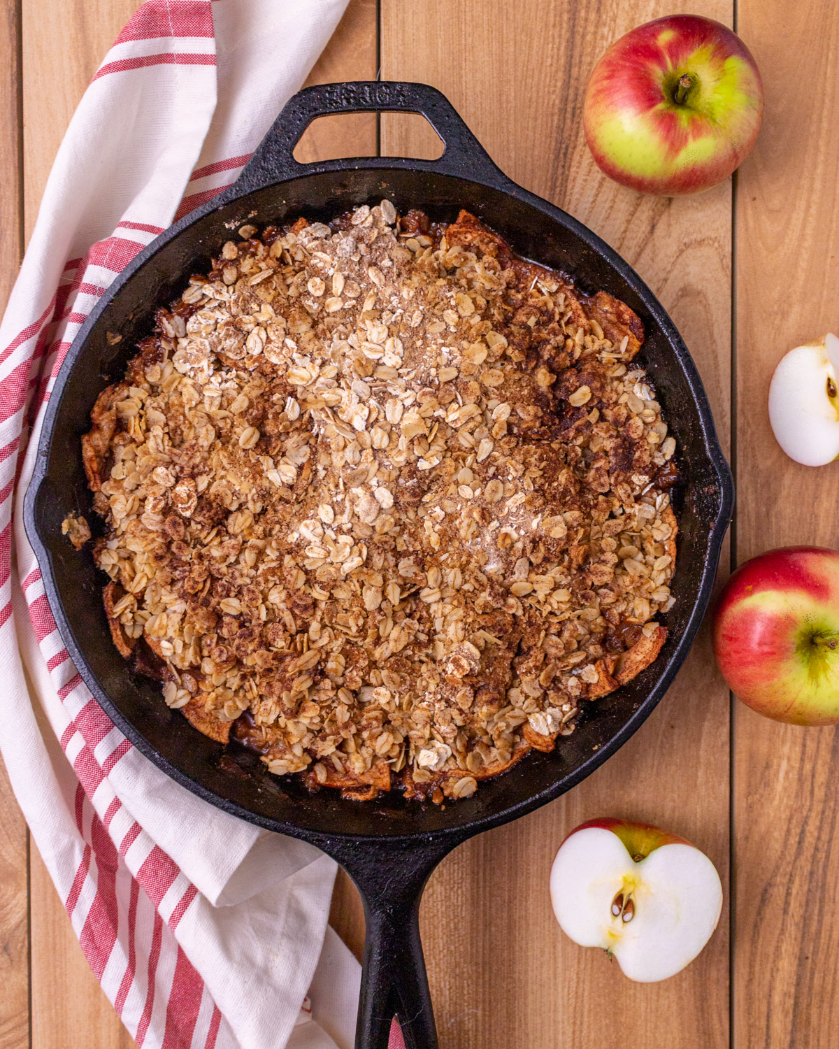 Baked apple crisp in a cast iron skillet with a red and white napkin and cut up raw apples.