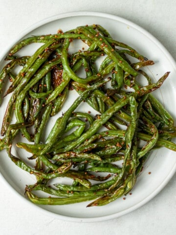 Cooked green beans on a white plate, tossed in whole grain mustard and honey.