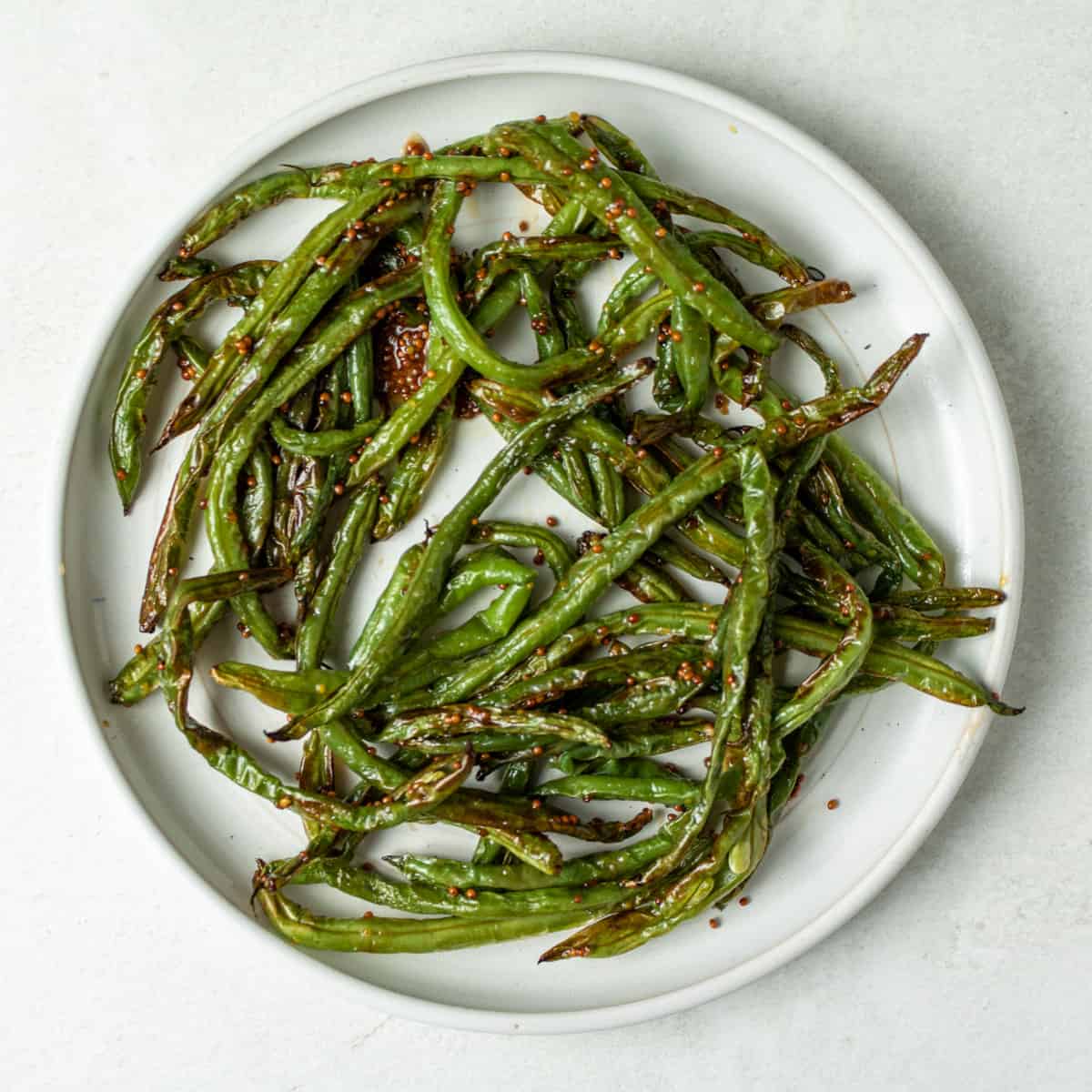 Cooked green beans on a white plate, tossed in whole grain mustard and honey.