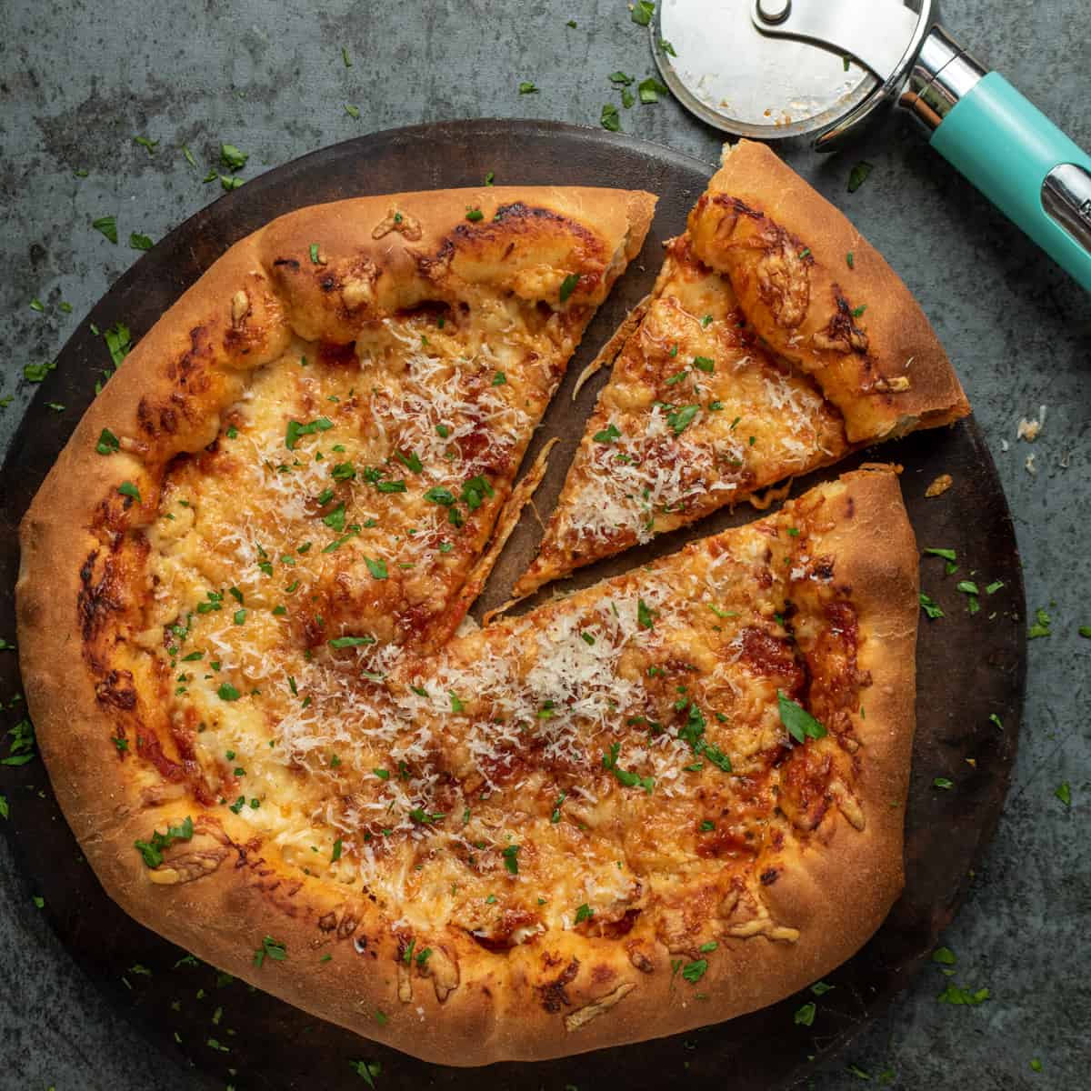 A fully cooked pizza on a pizza stone with one slice cut out. The one slice is slightly pulled out. In the corner of the photo is the pizza cutter. 