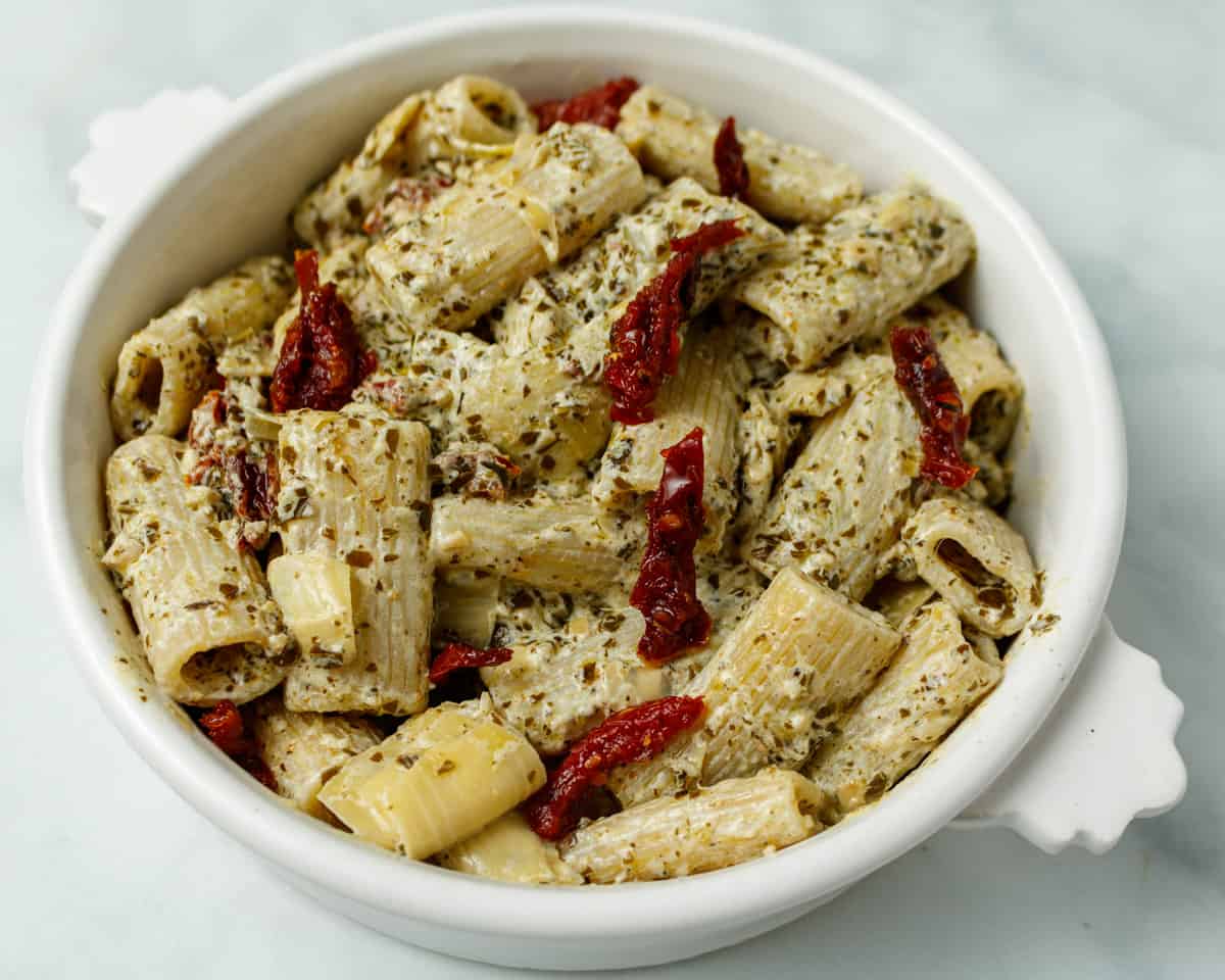 Top down photo of creamy pesto in a white bowl on a white marble background.