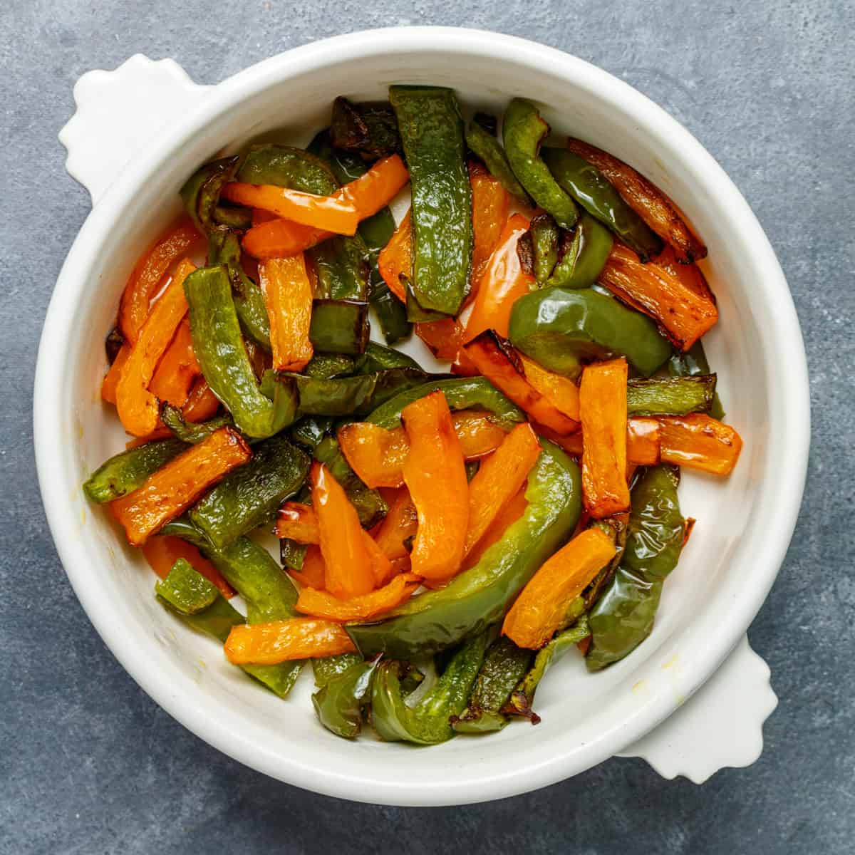 Cooked green and orange bell peppers in a white serving dish.