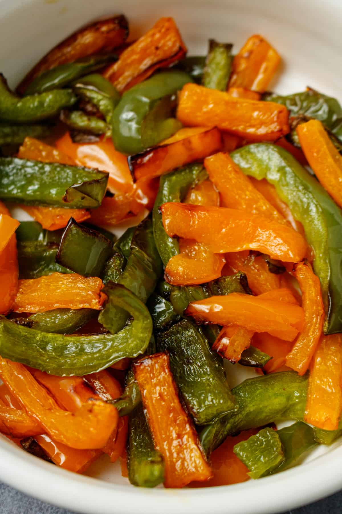 A close up of cooked green and orange bell peppers in a white serving dish.